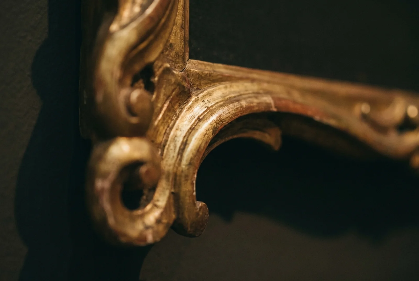 Close-up of a hand-carved wood detail with gilded edge in museum lighting.